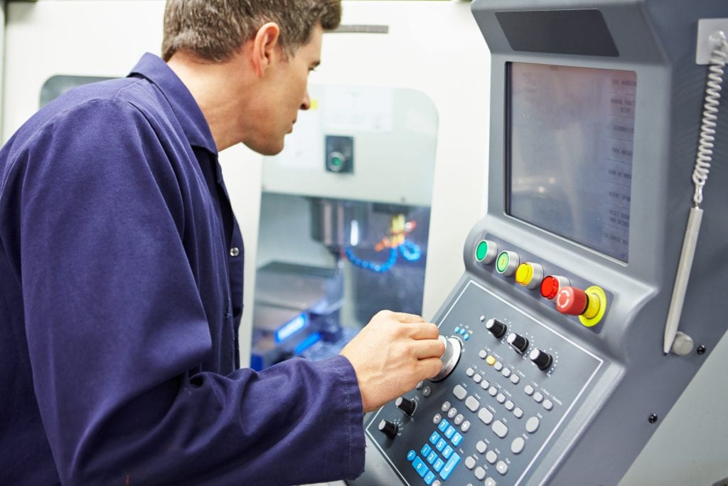 Man standing in front CNC milling machine control panel adjusting dials