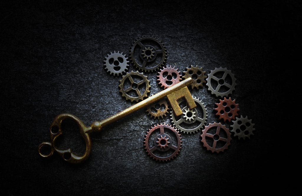 Antique key laying on vintage metal gears on a dark background