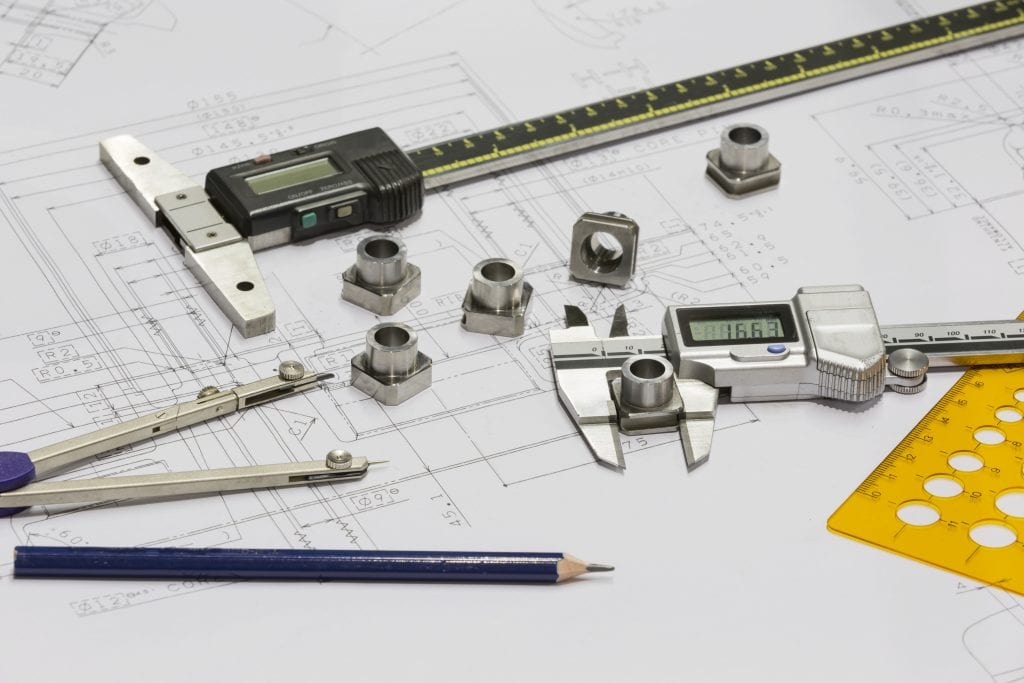 Digital calipers, protractor, lead pencil, small machined parts laying on engineering drawing